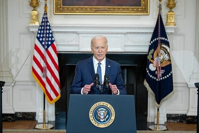 Biden standing before a podium at the White House and speaking.