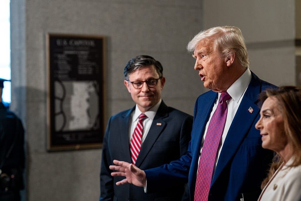 President Trump speaking and gesturing to the press next to House Speaker Mike Johnson, standing next to him and looking on