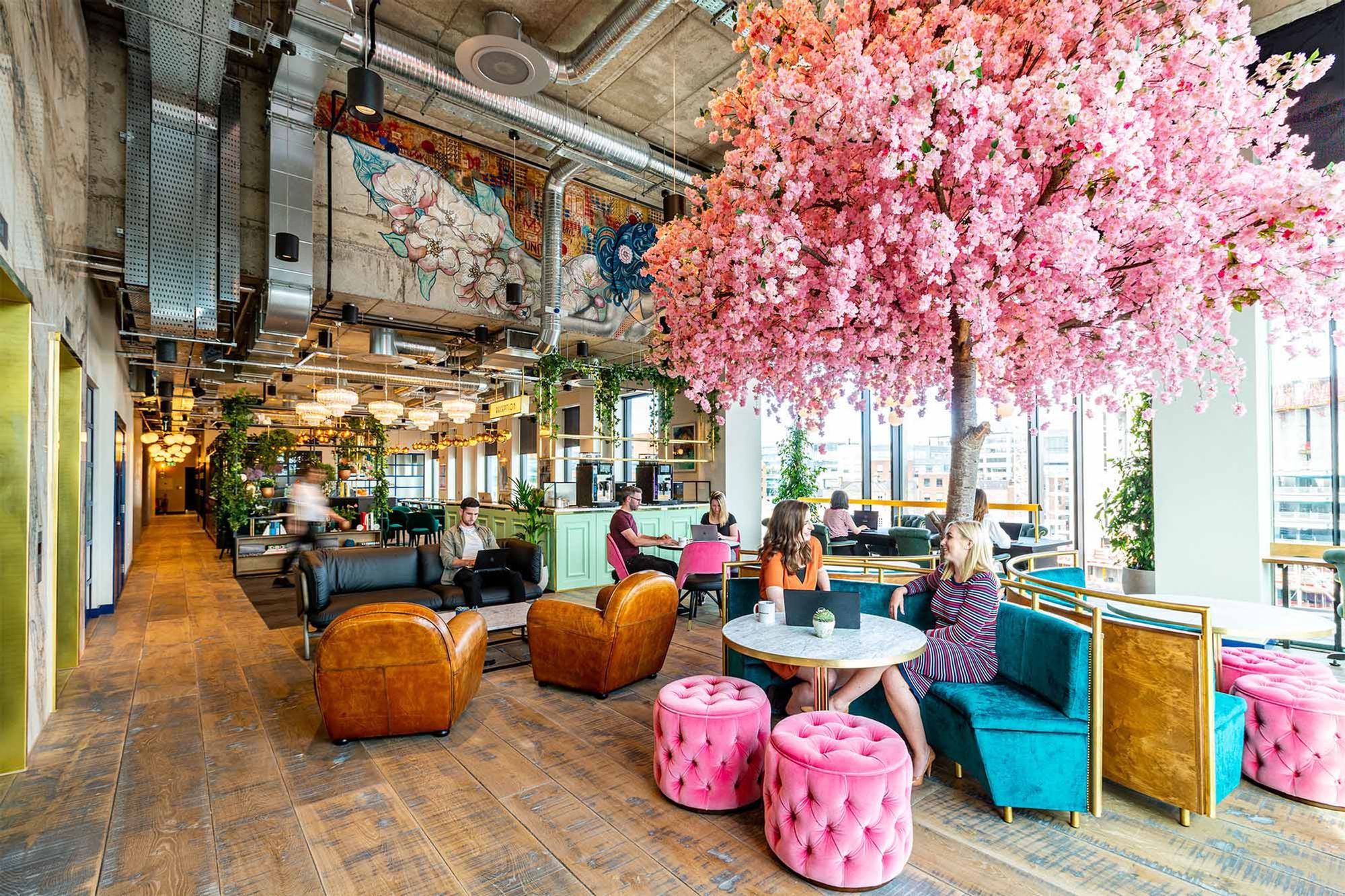 Cafetería de Iconic Offices con mesas sofas y un arbol rosa