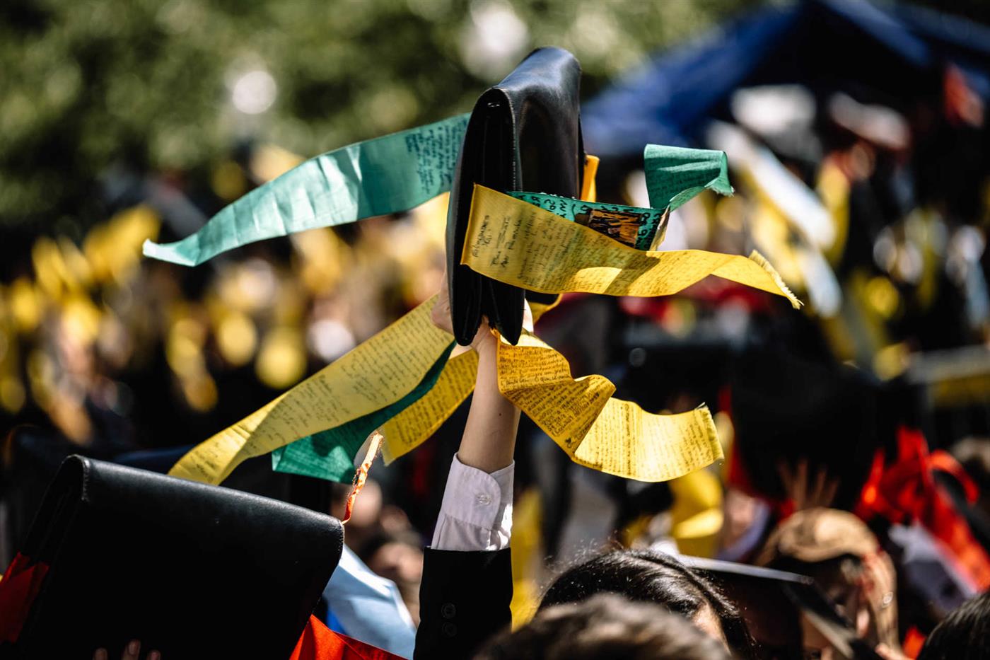 Braço levantando um boné de estudante com citações costuradas nele