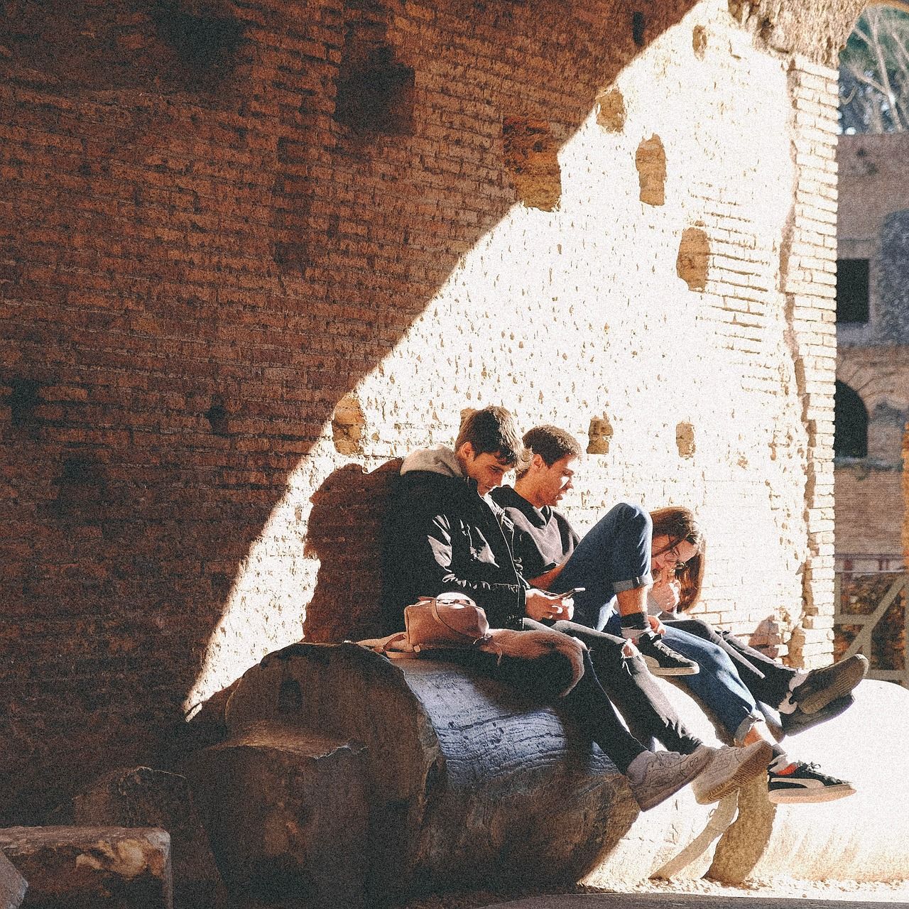 Três jovens sentados debaixo de um muro em Roma