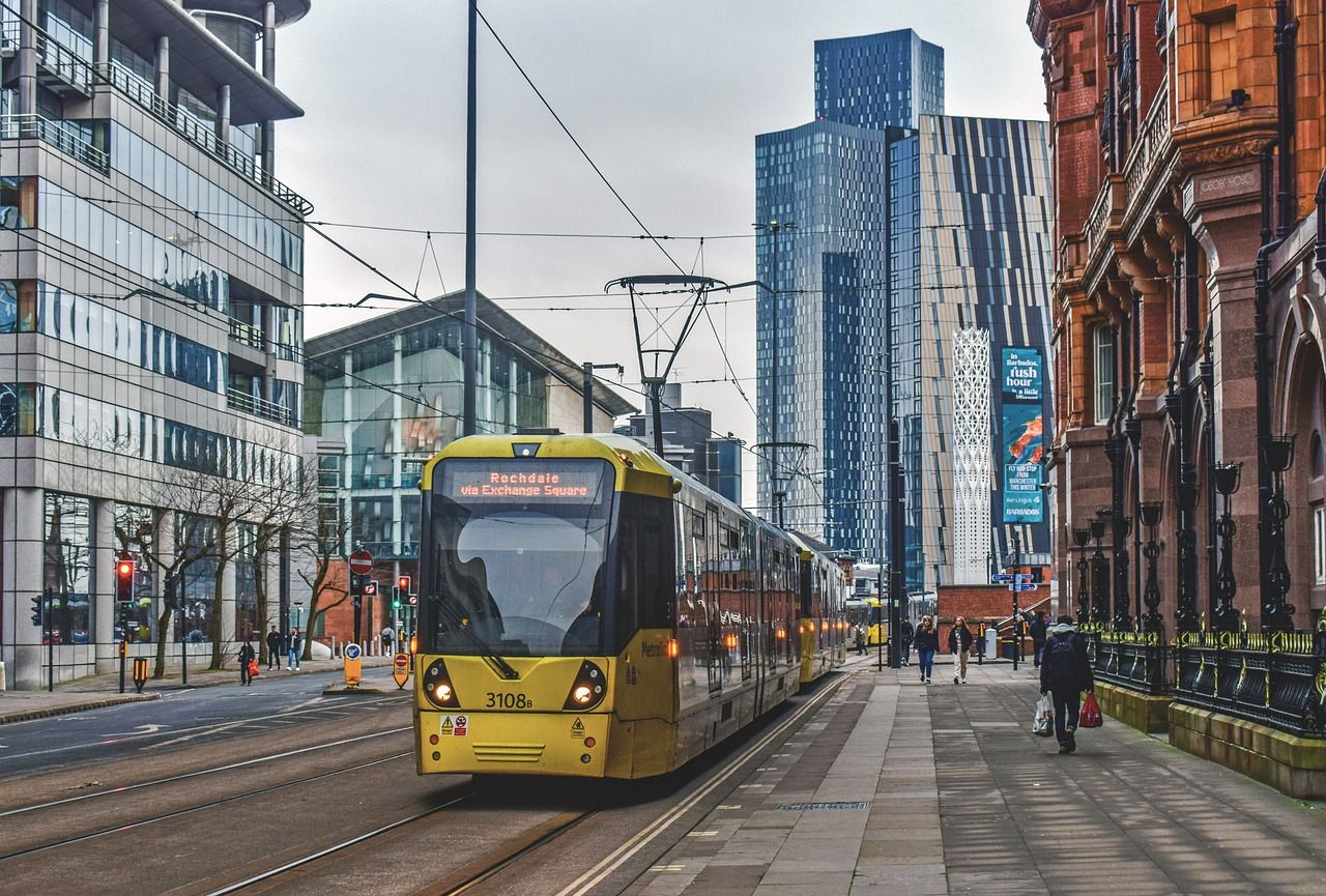 Rame de tramway jaune de Manchester, avec une bâtisse typique en brique rouge à droite et des gratte-ciels modernes au fond