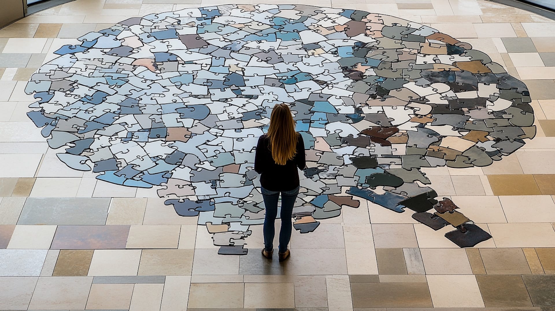 A woman standing by a giant jigsaw puzzle of the human brain.