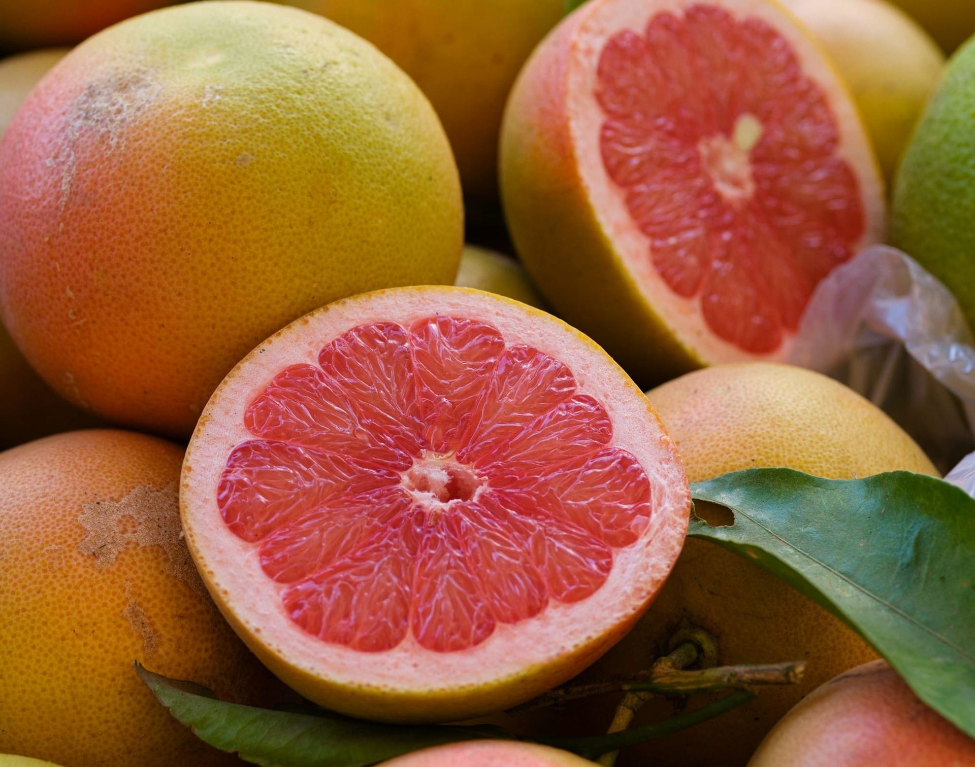Whole and halved pink grapefruit with rosy flesh piled together with green leaves