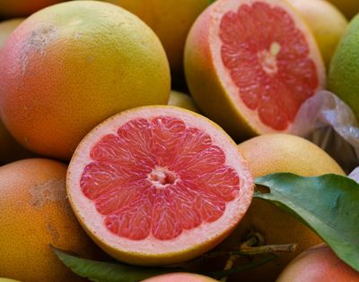 Whole and halved pink grapefruit with rosy flesh piled together with green leaves