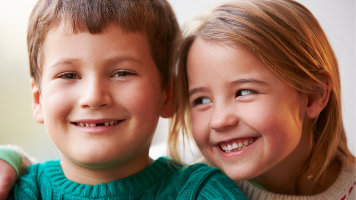 Two children smiling, one child is looking at the camera the other is looking at the other child