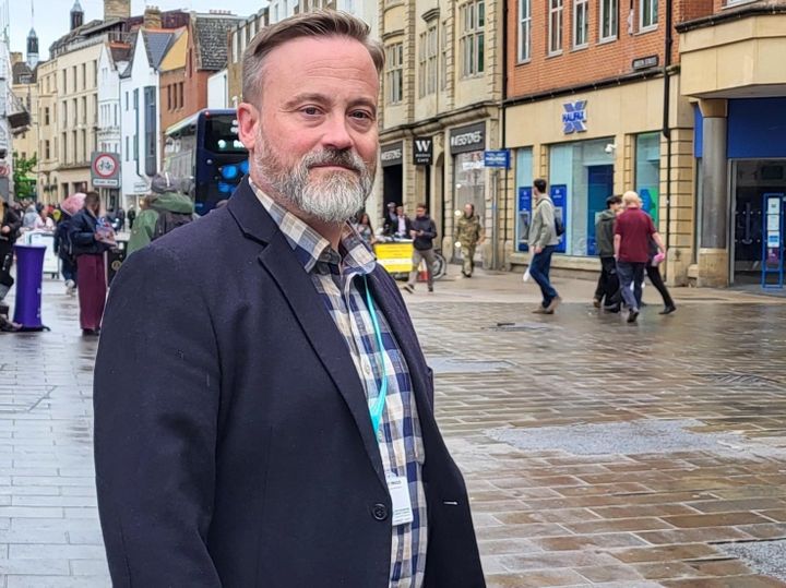 A man standing in a busy street with shoppers behind him