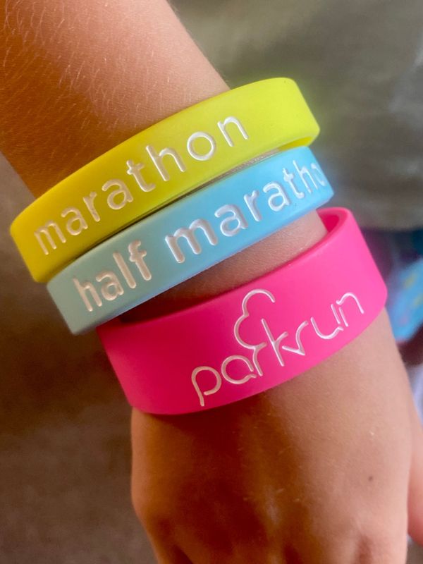 A child’s wrist, wearing a Parkrun wristband along with marathon and half-marathon bands