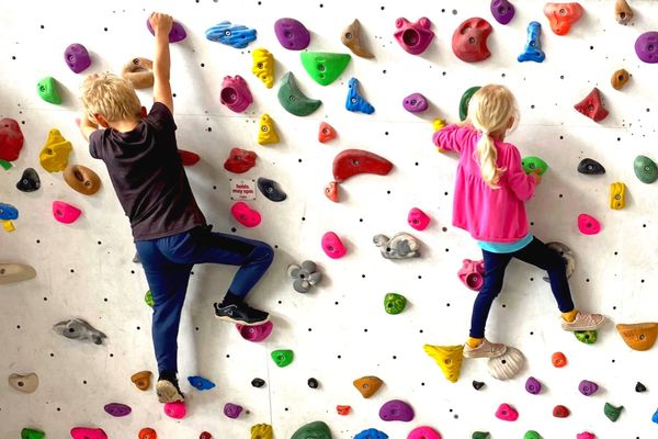 A young boy and girl gripping on to a bouldering wall with colourful grips.