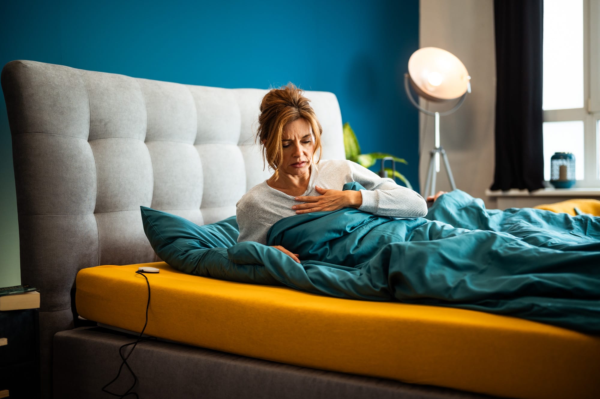 Frau sitzt unruhig im Bett mit Hand auf der Brust – Symbol für die Folgen von schlechtem Schlaf oder Schlafmangel.
