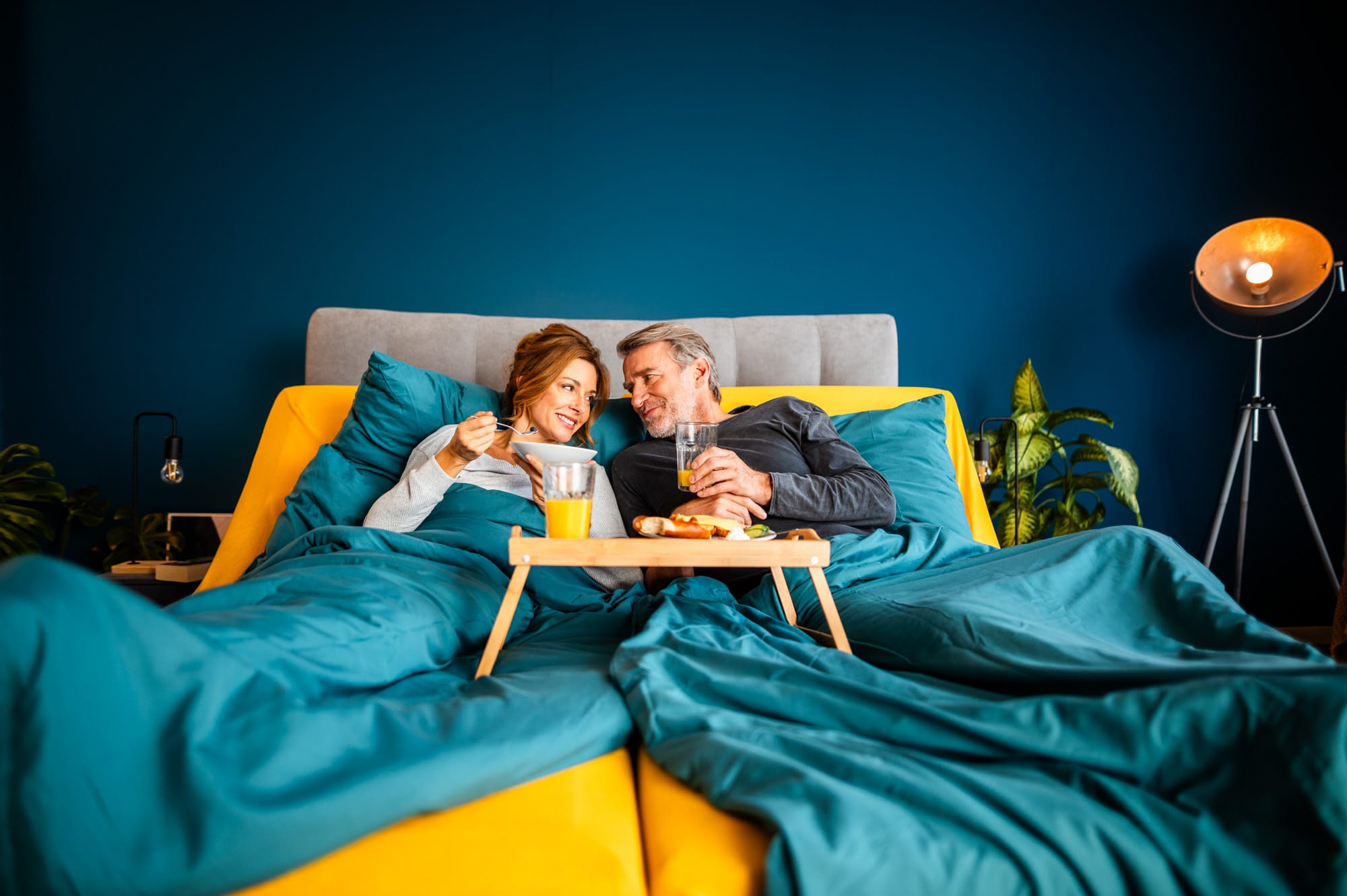 Paar liegt entspannt in einem Bett mit dem CosyLift und frühstückt gemeinsam in erhöhter Position