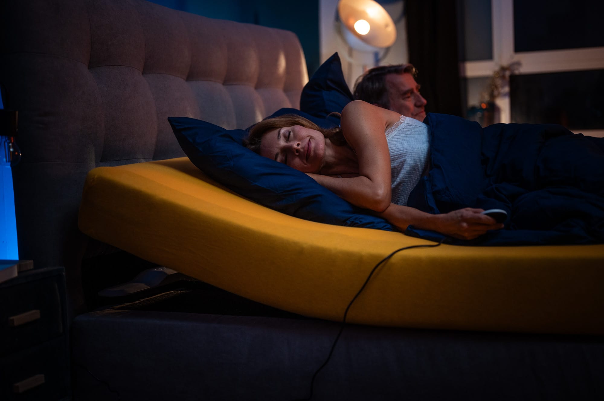 Frau schläft auf einem Bett mit dem CosyLift, der die Matratze elektrisch anhebt, während ein Mann daneben liegt