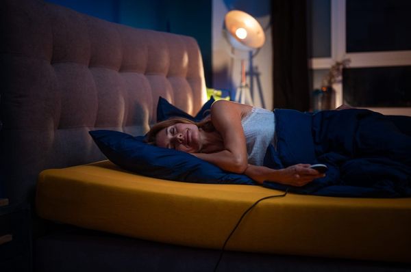 Frau liegt entspannt auf der Seite in einem modernen Bett mit verstellbarer Matratze und Fernbedienung – gemütliche Schlafumgebung mit warmem Licht.