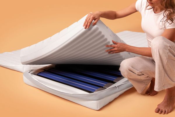 Frau hebt Bezug einer Kaltschaum Matratze an und zeigt den inneren Aufbau mit Schaumkern und Lattenrost.