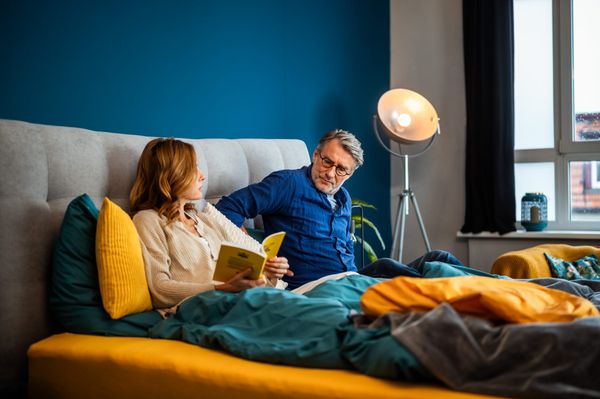 Paar sitzt entspannt im Bett und liest – Symbol für rückenschonenden Schlaf und ergonomische Matratze.