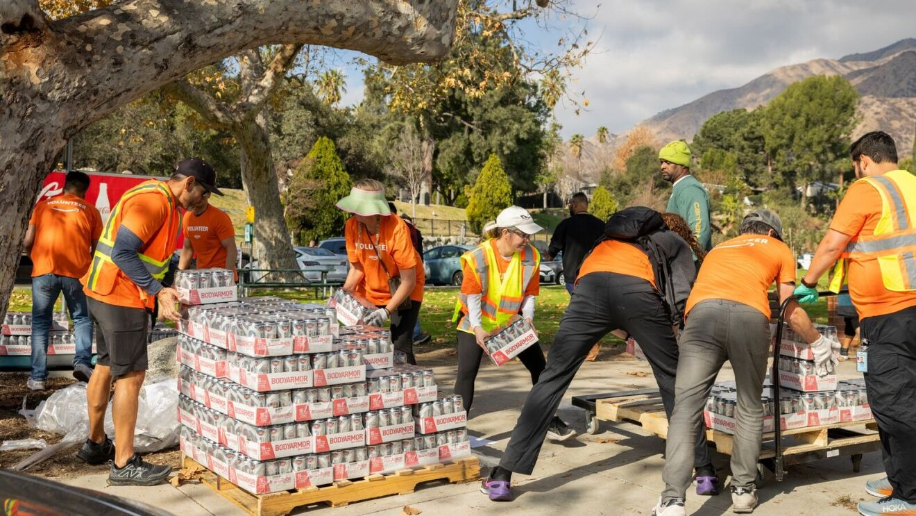 Amazon volunteers in orange safety vests distributing pallets of bottled water in a park in California for wildfire relief.