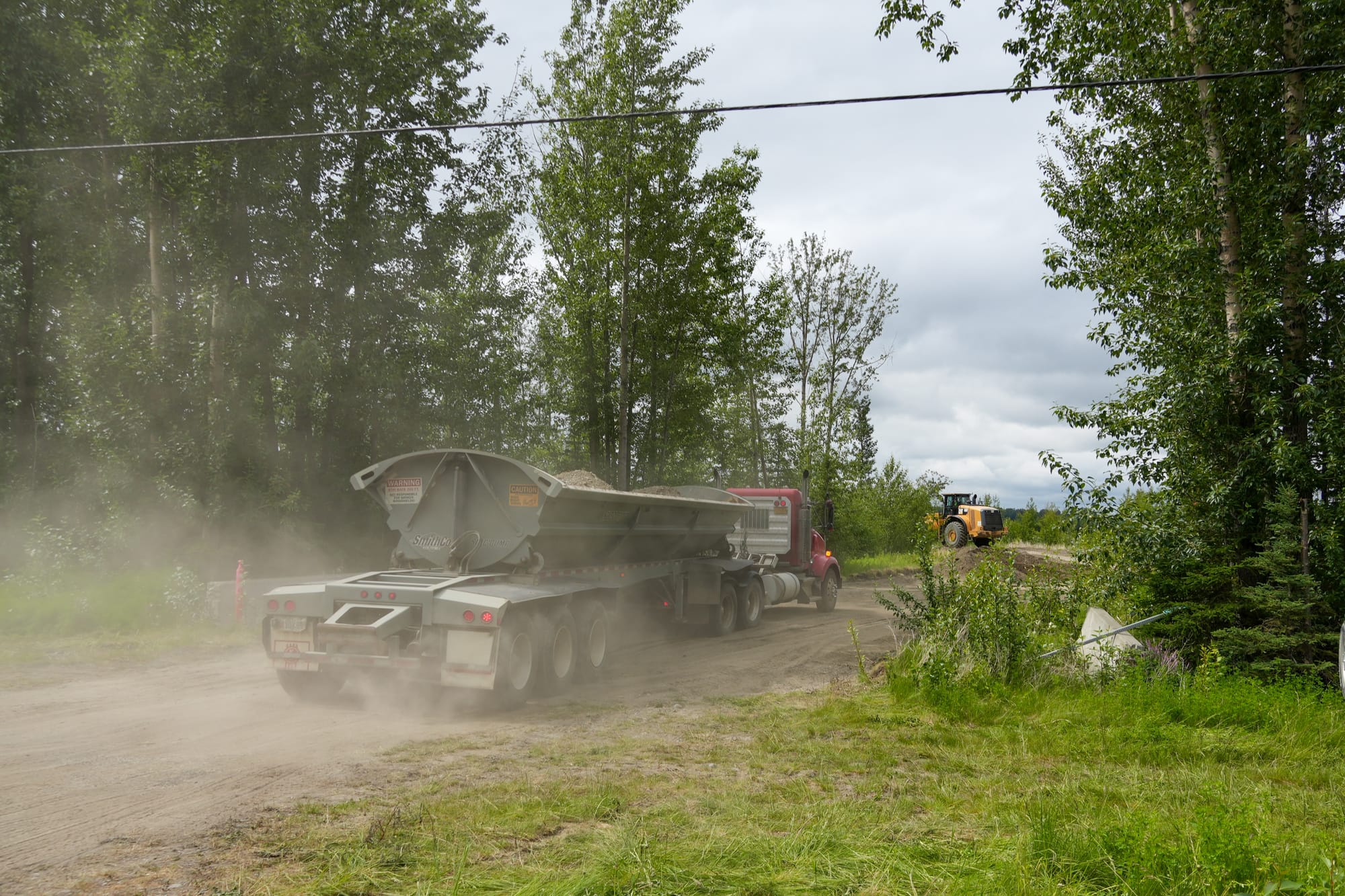 A dump truck transports gravel into a staging area just off the Matanuska River