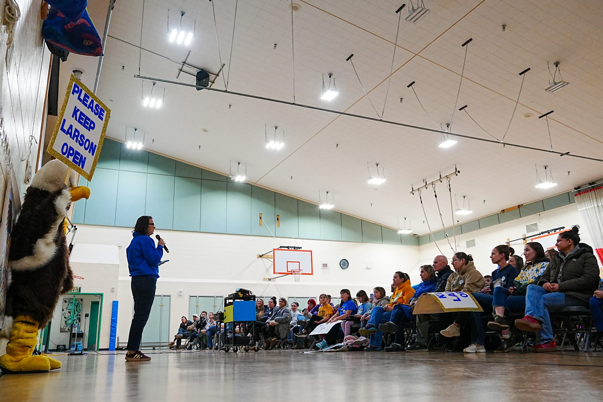 A former Larson Elementary School student holds a "Please Keep Larson Open" sign as Family Teacher Association President Alyson Coffman speaks