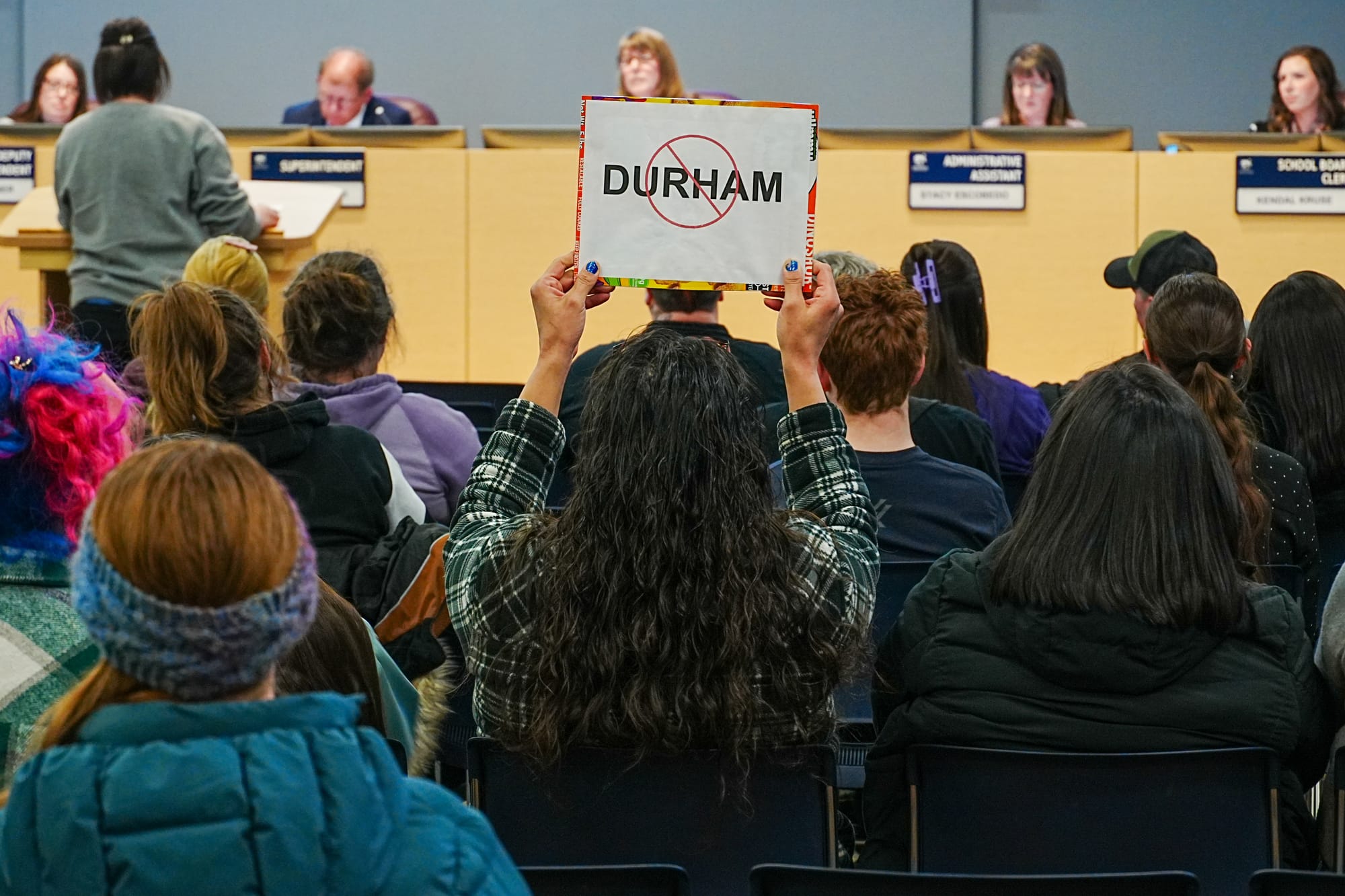 A community member holds up a sign during a Matanuska-Susitna Borough School Board meeting