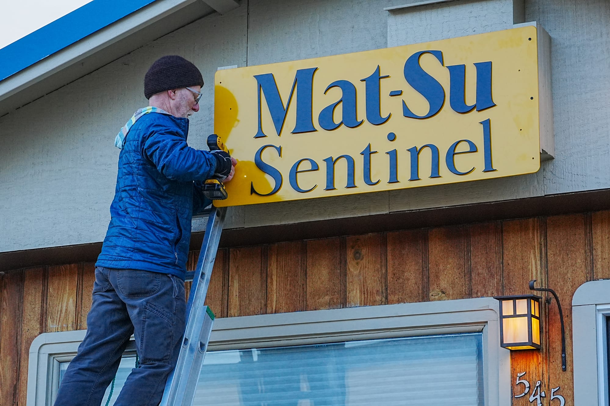 Mat-Su Sentinel board president Steven Merritt bolts the Sentinel's sign to the building.