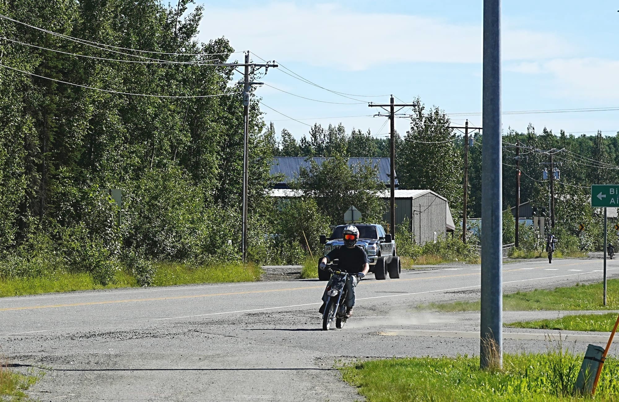 A person drives a dirt bike down a bike path along Big Lake Road