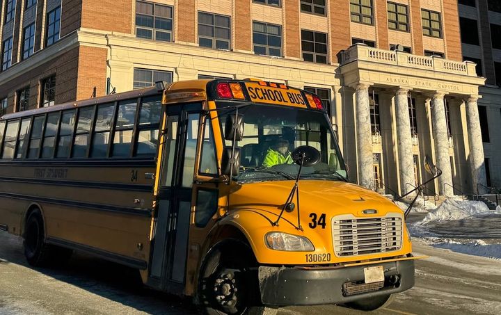 A school bus drives in front of the Alaska State Capitol