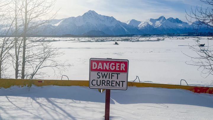 A danger sign and snow-covered barriers sit against the Matanuska River bank near Palmer on March 16, 2025.