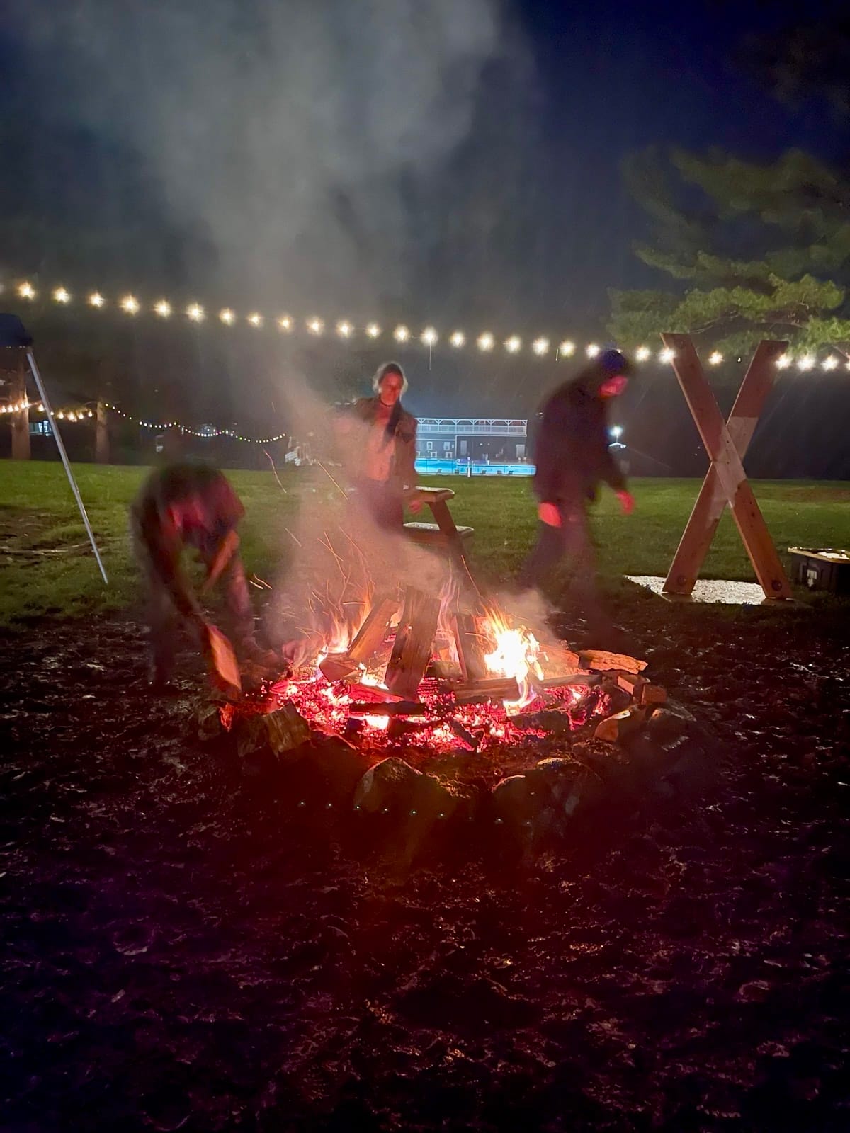 a man adds wood to a burning fire while a woman dances behind it