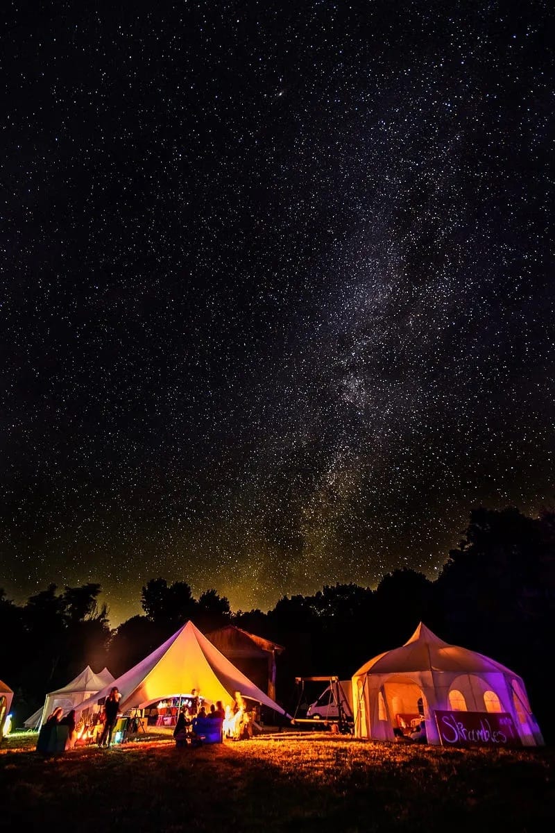 The night sky and milky way above colorful tents at a burn