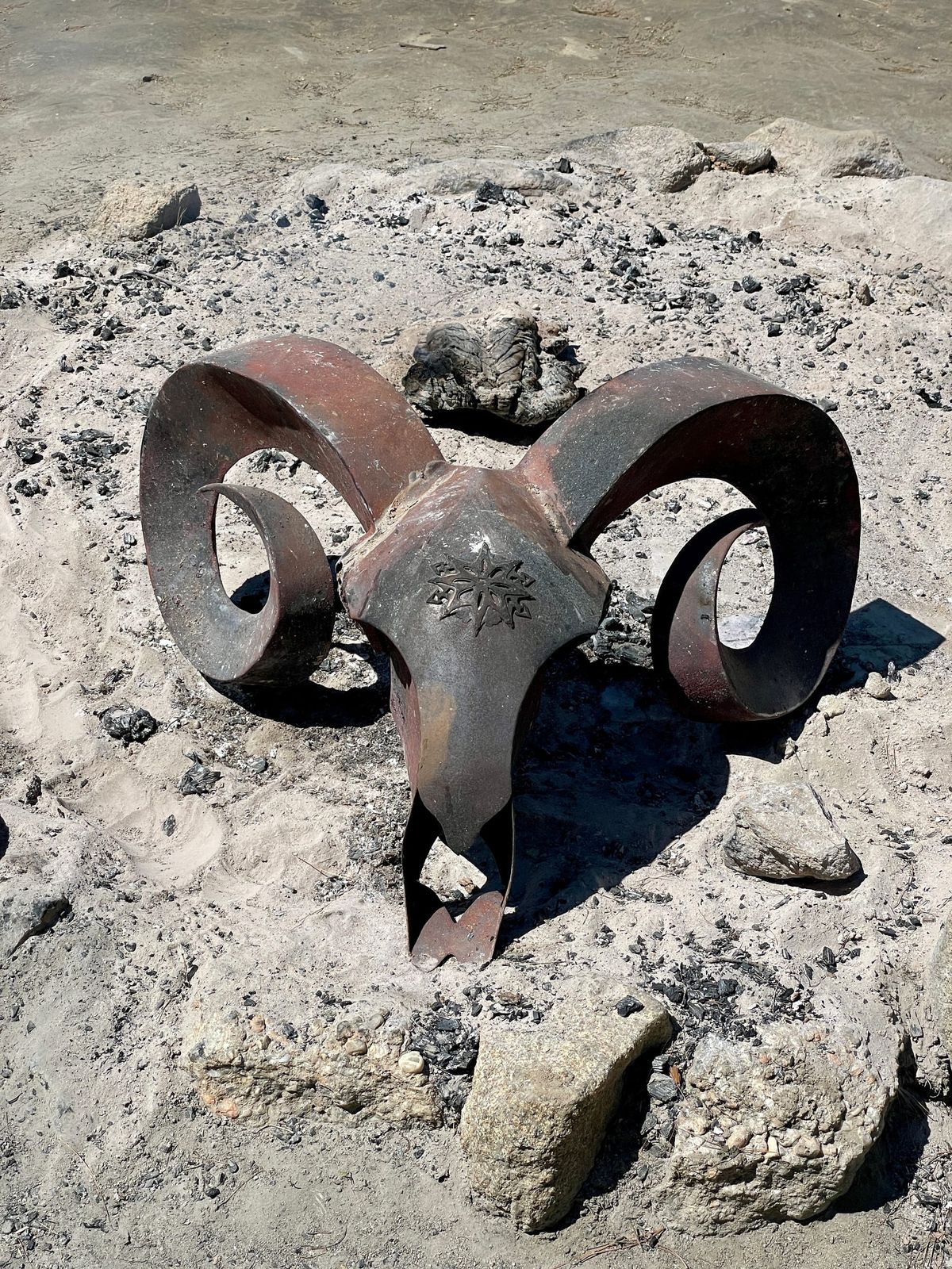 A large metal ram's head in the ash from a fire
