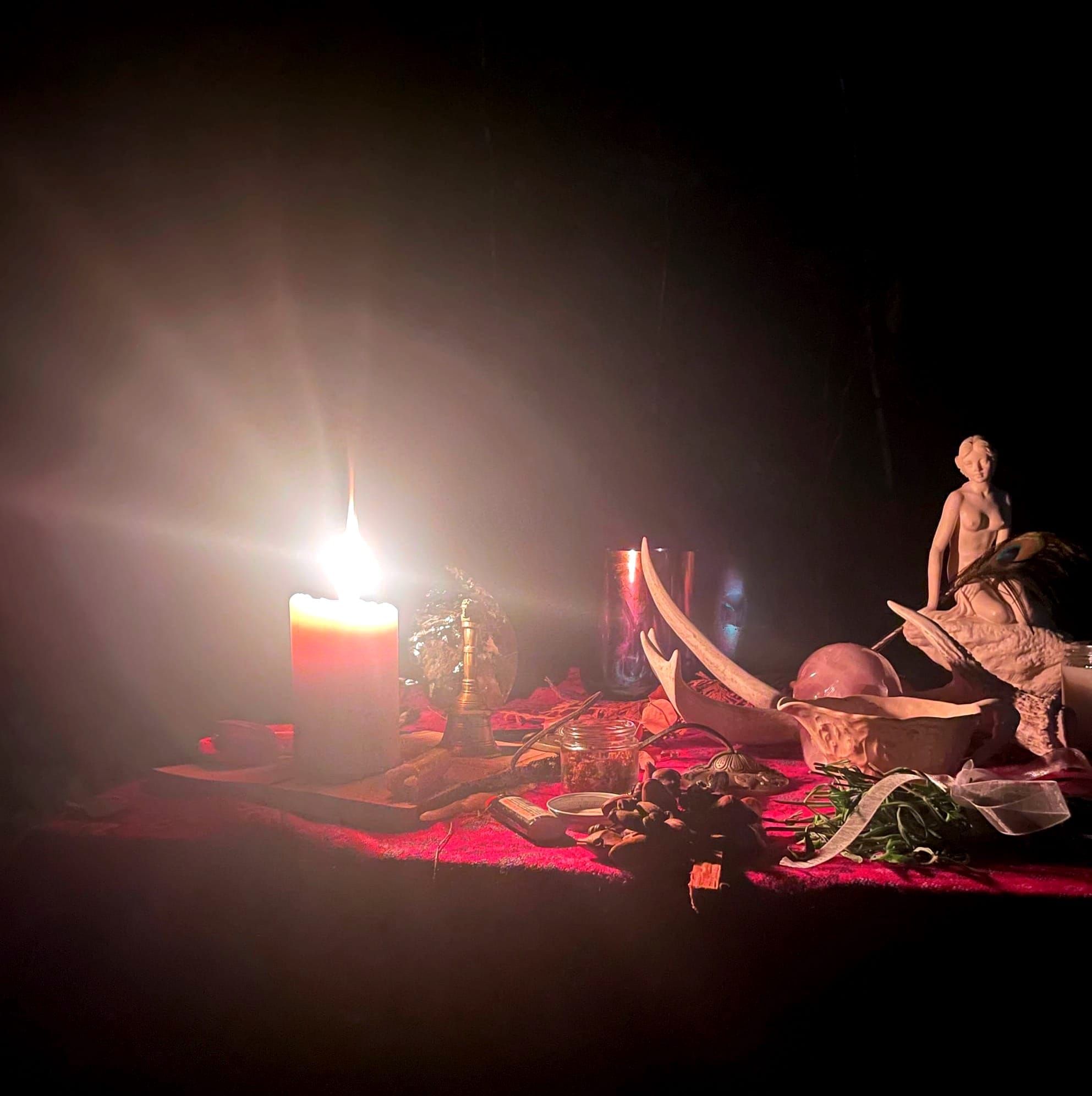 An altar with a candle, herbs, a goddess statue and antler. 