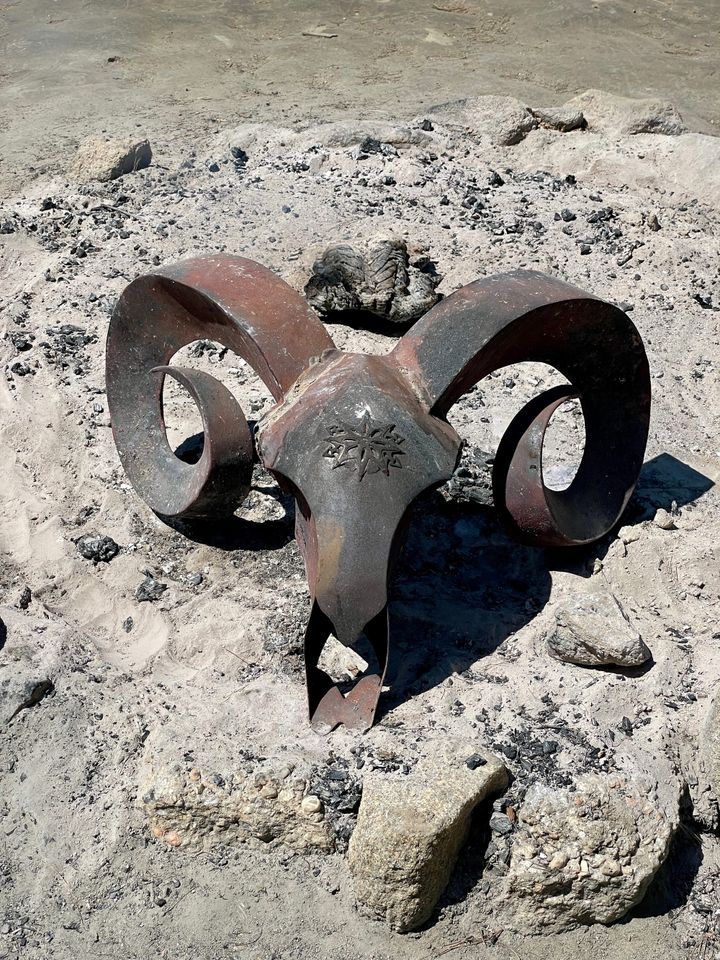 A large metal ram's head in the ash from a fire