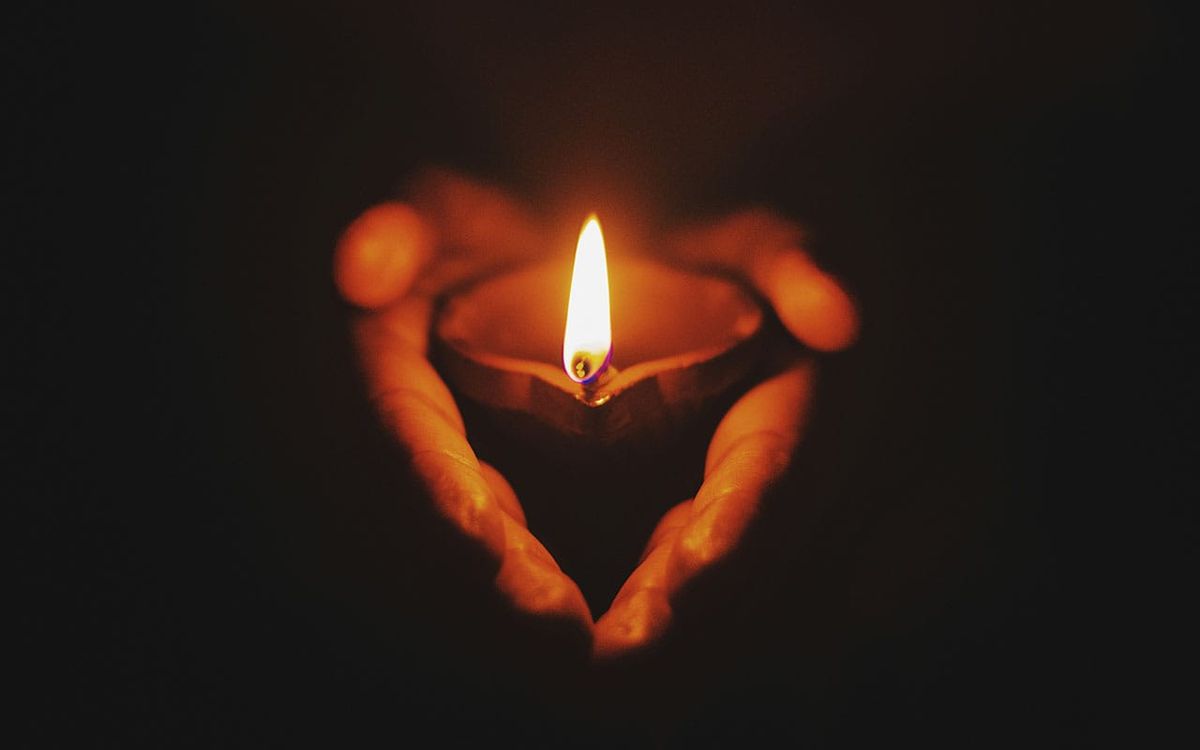 Hands gently holding a single candle flame in the darkness, symbolizing inner light, life’s sacredness, and the spiritual call to dissolve the ego rather than destroy the body.