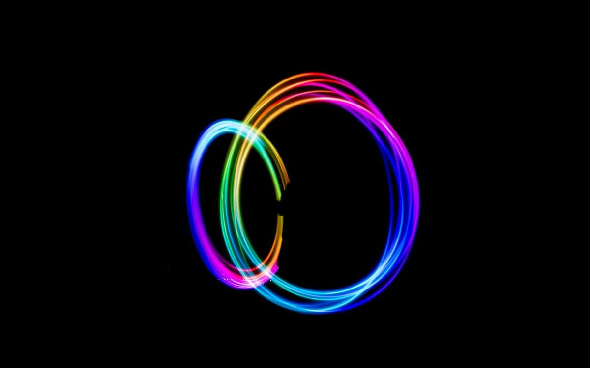 Person spinning poi with vibrant rainbow light trails forming circles in long-exposure time-lapse at night