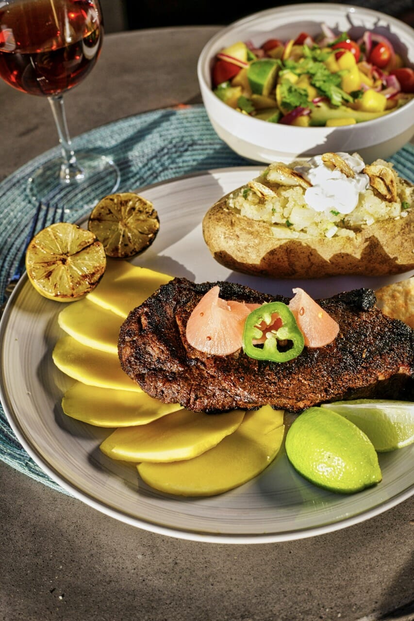 Steak cubain, mangue en tranches et citronsvverts. 1 pomme de terre farcie et une petite assiette de salade derrière