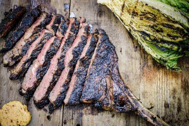 Tomahawk grillé et tranché, rosé, une rondelle de beurre en-dessous et une demi laitue romaine grillé au-dessus