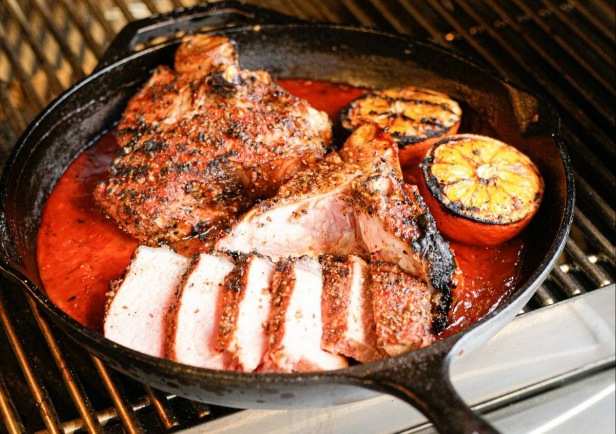 Dans une poële en fonte, un fond de sauce à l'orange, 2 oranges grillées et 2 T-Bones de veau tranchés