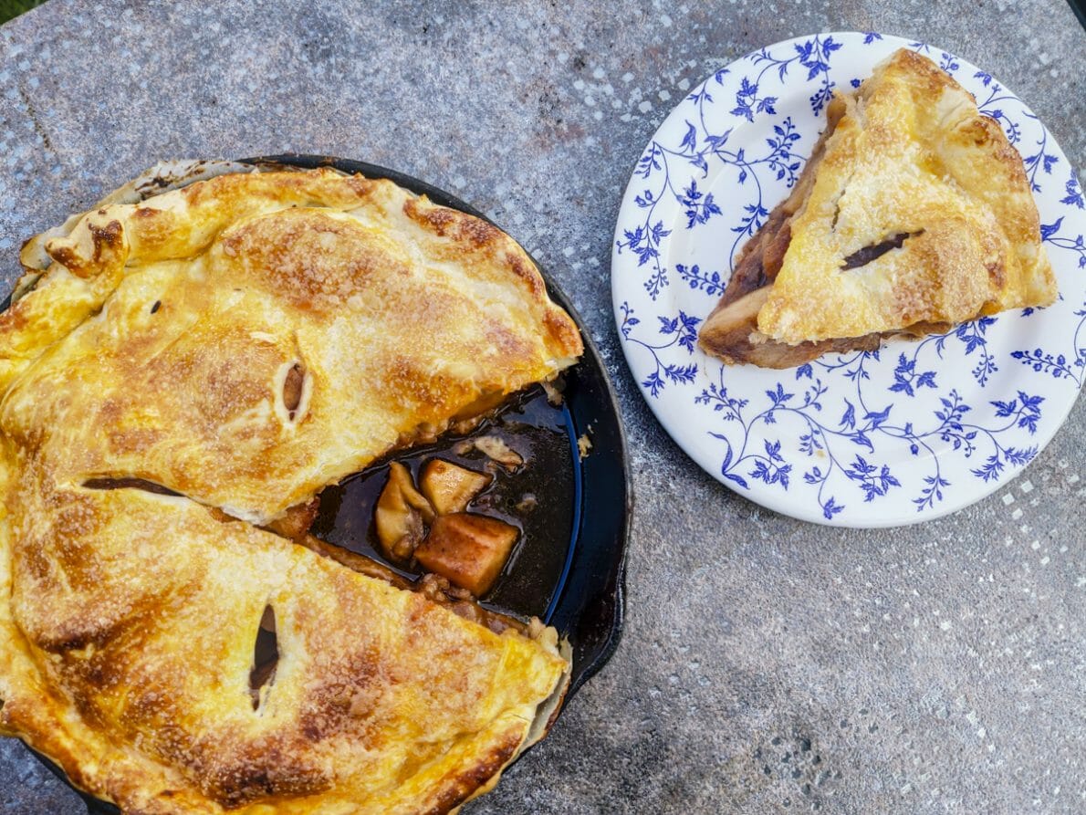 fond gris, une tarte aux pommes recouverte, il manque un morceau. Ce morceau est dans une assiette blanche et bleue sur le côté.