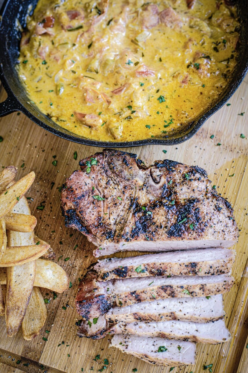 Une grosse côte de porc grillée et tranchée, des frites et une poêle en fonte pleine de sauce