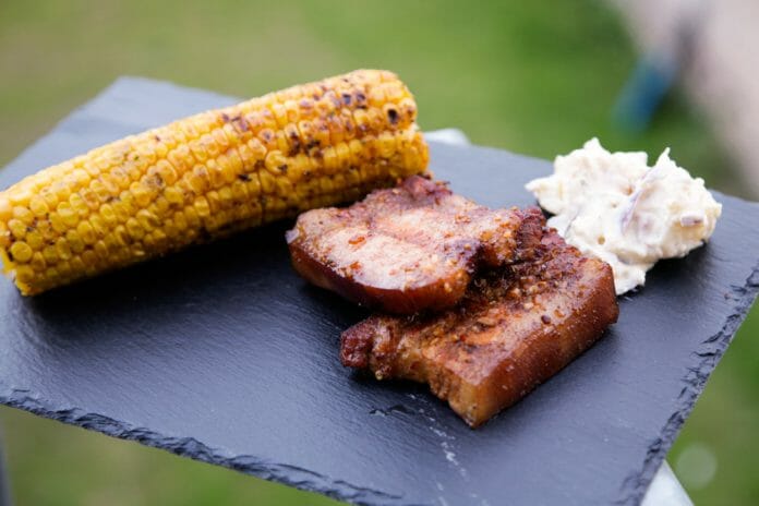 Ardoise avec 2 tranches de lard fumé, un épis de maïs grillé et de la salade de pommes de terre.