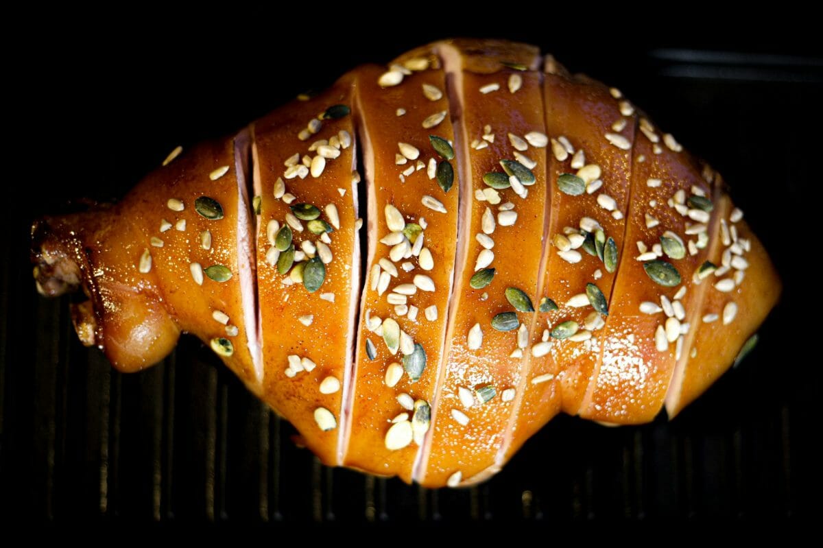 Sur un fond noir, un jambon de Noël entier glacé, avec des graines parsemées dessus