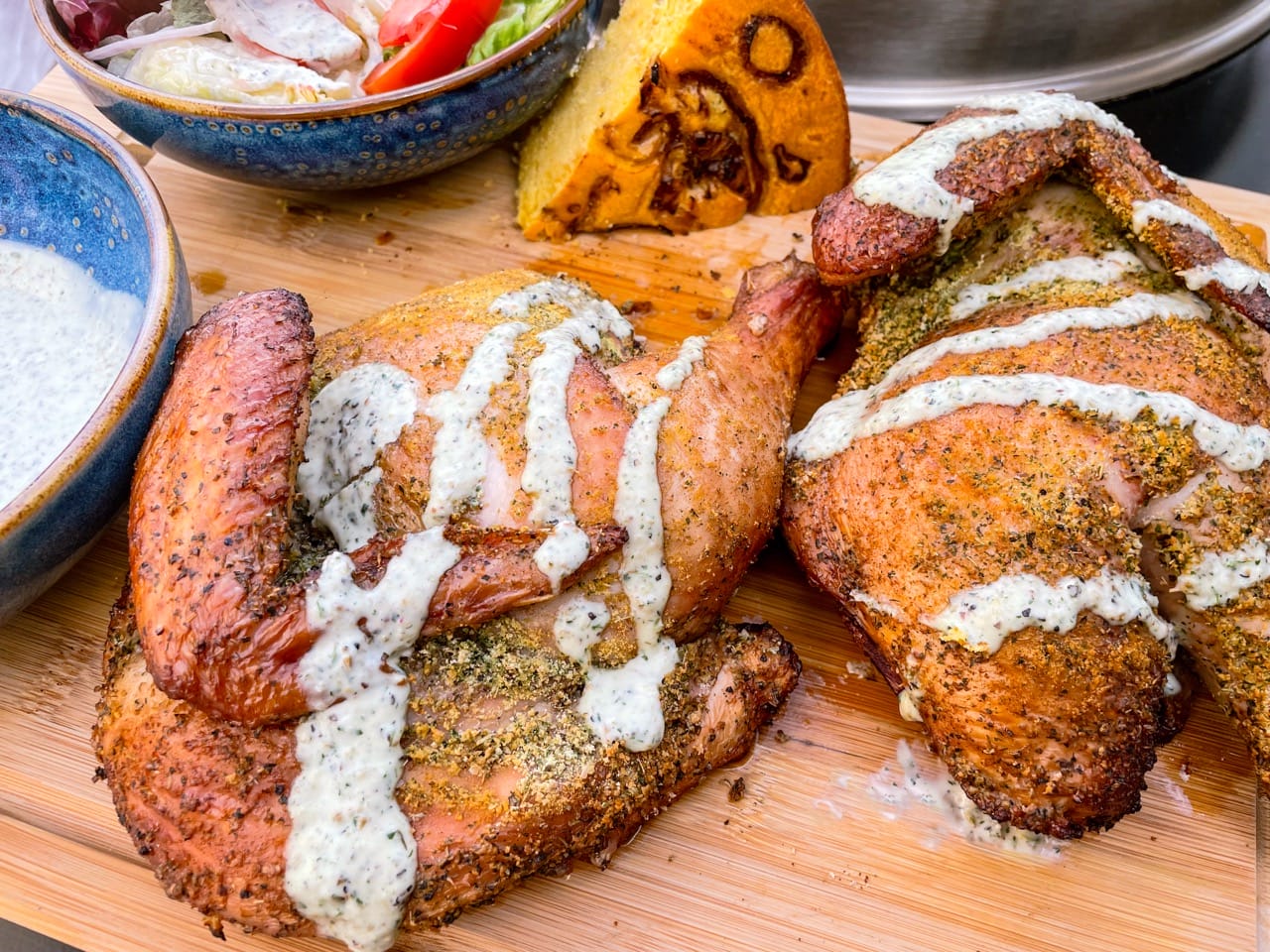 Gros plan sur un poulet coupé en 2 sur une planche, arrosé de sauce Ranch. A l'arrière une portion de pain de maïs aux oignons