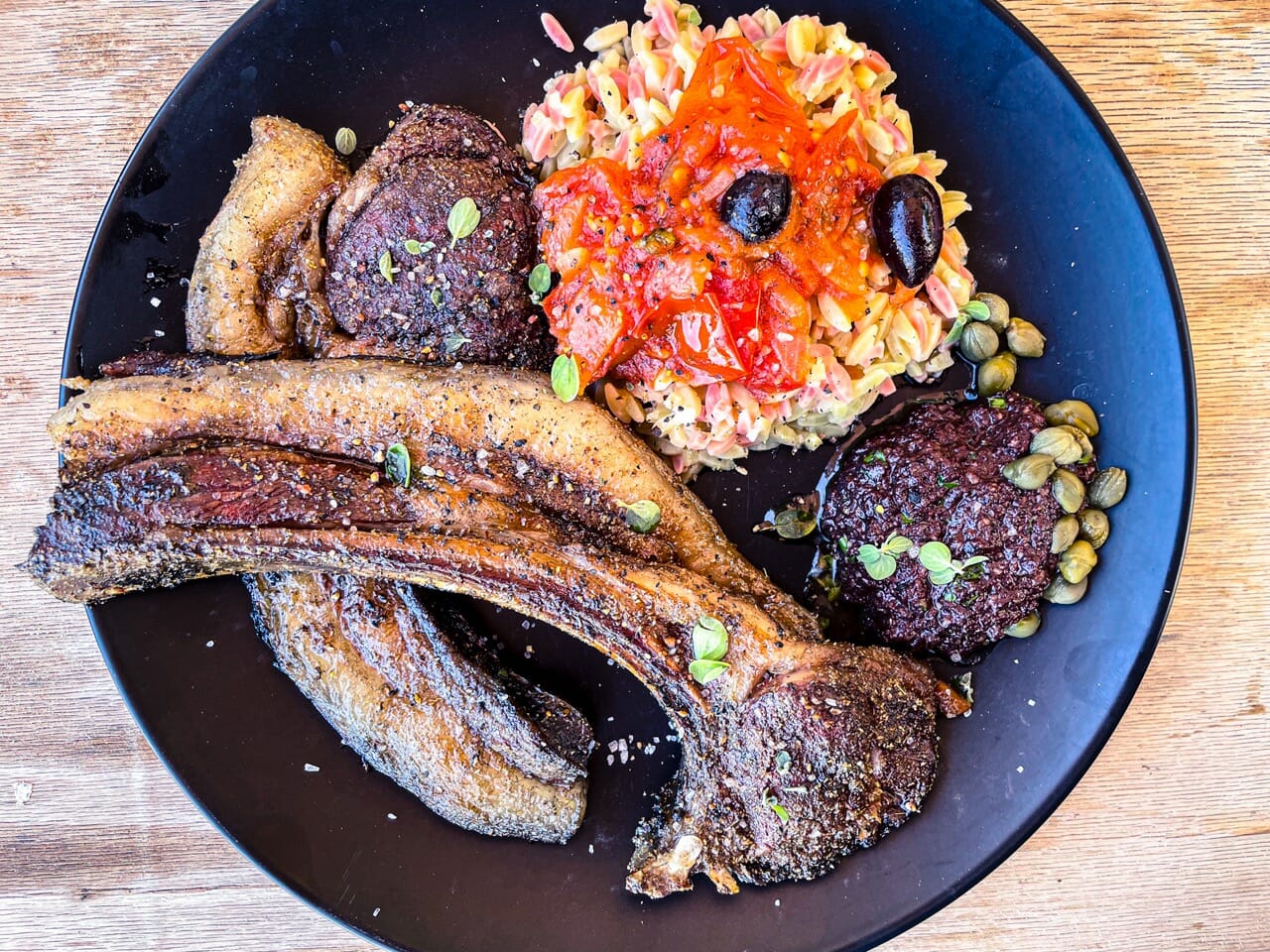 2 belles côtes d'agneau grillées avec de la tapenade d'olives noires, de l'orzo et de la tomate.