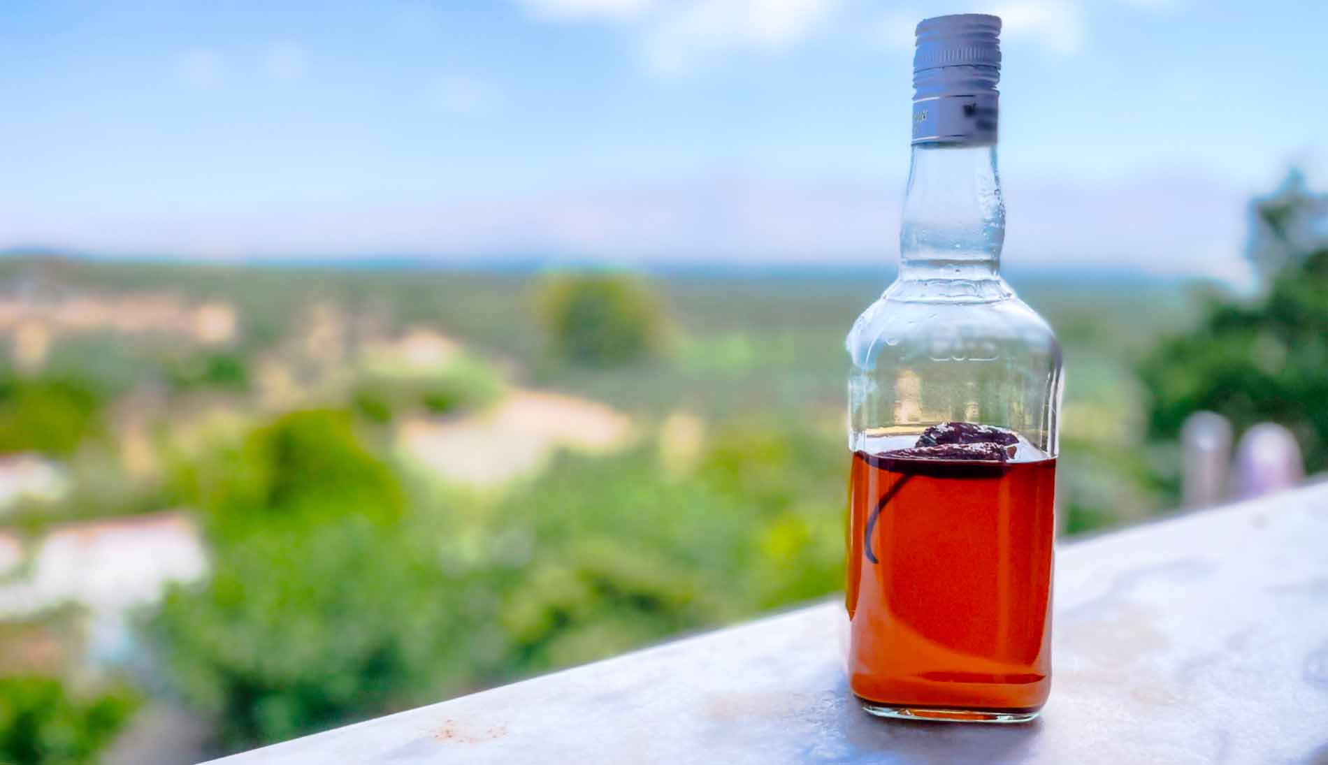 Une bouteille type bourbon remplie d'huile piquante fumée sur un balcon avec un beau décor derrière
