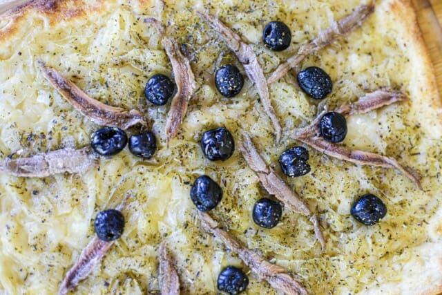 Gros plan sur une pissaladière. On voit bien les anchois les oignons et les olives.