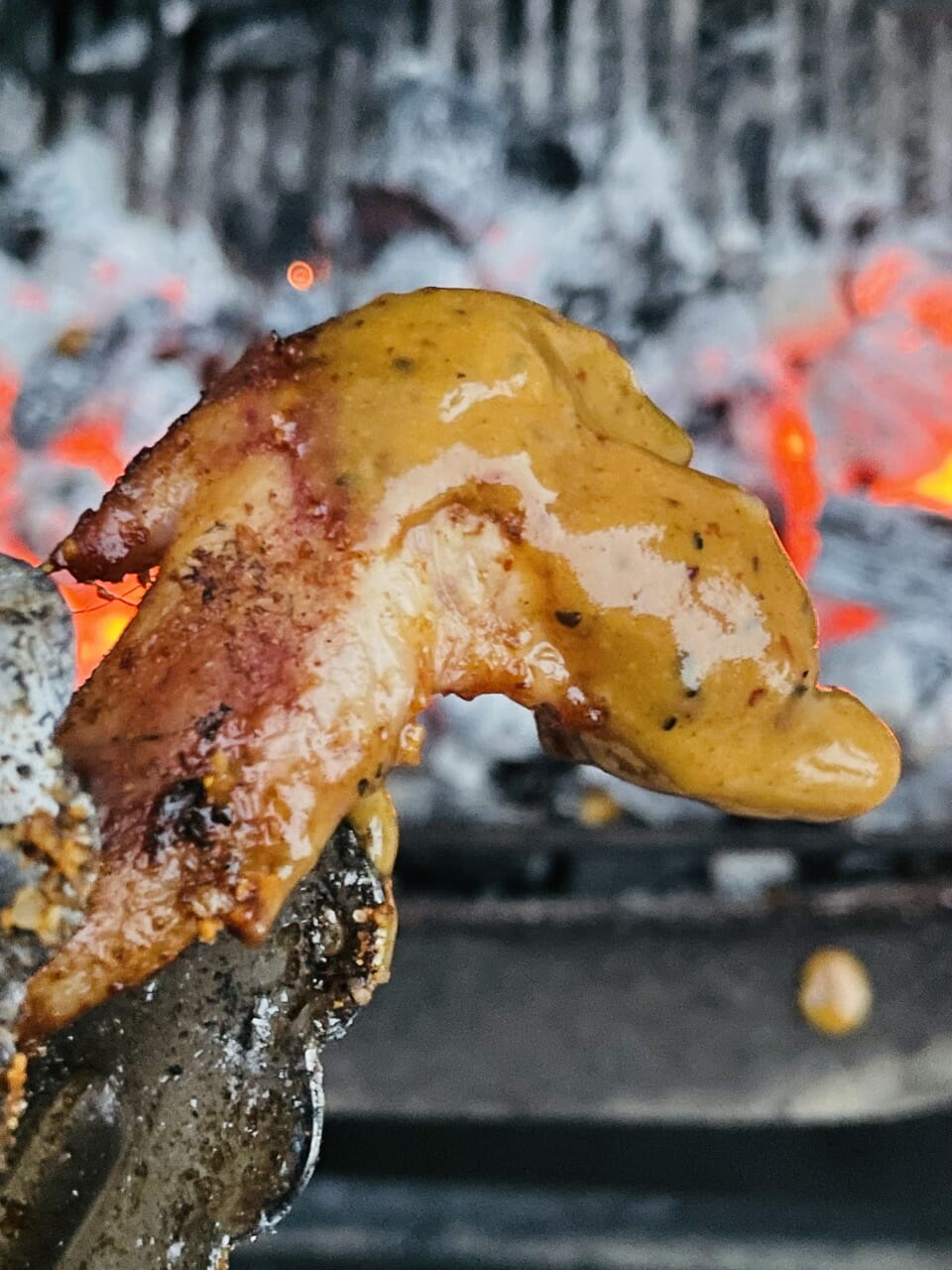 gros plan sur une aile de poulet recouverte de la sauce BBQ érable et Chipotle.Des braises rouges en arrière plan