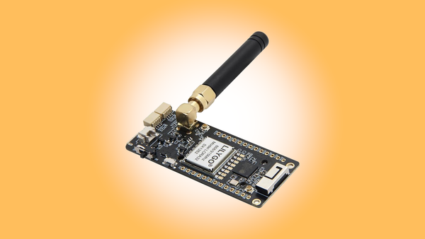 The Lilygo T3 S3 device with an attached antenna on an orange background with a white fuzzy circle at the center.