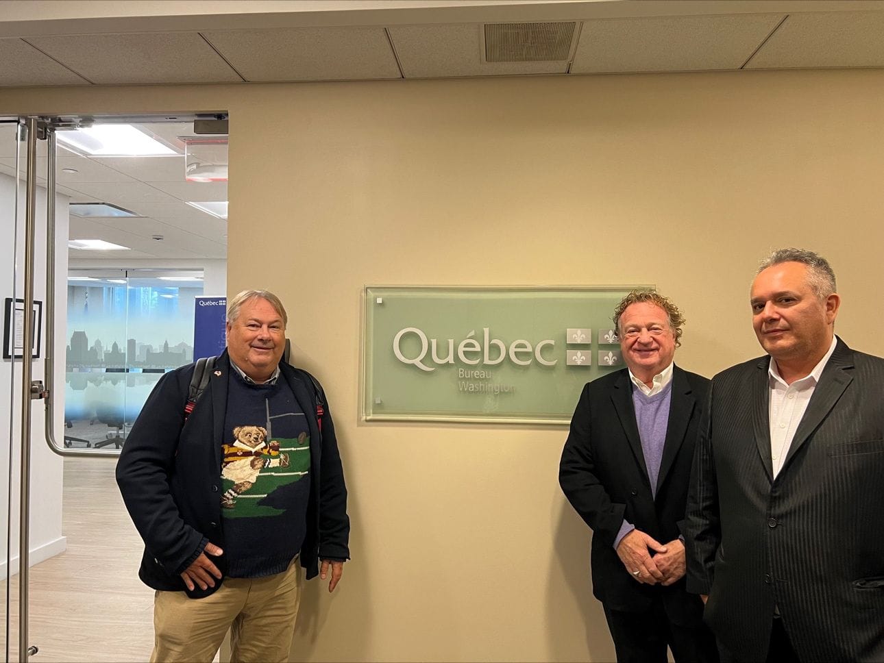Three men pose for a photo in front of a province of Quebec sign.
