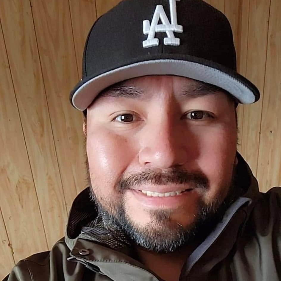 Elias Whitehead is smiling. He has a short beard and is wearing a black hat.