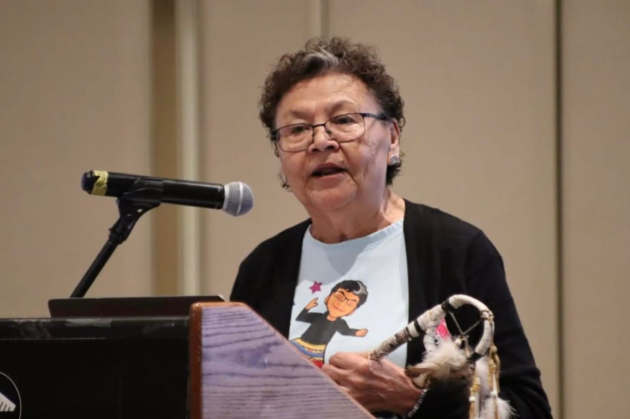 An elderly women speaks at a podium in front of a microphone